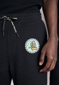 Pantalons de survêtement noirs texturés avec un patch en forme de logo circulaire de gelato sur la poche, dotés de cordons de serrage ajustables et de pointes de marque.