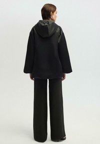 Felpa oversize nera con cappuccio in satin, abbinata a pantaloni neri a gamba larga. Tessuto morbido e design semplice, adatta per un look casual.