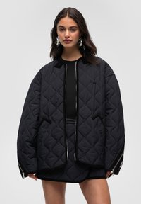 Giubbino imbottito nero con chiusura a zip, dettagli a coste, due tasche laterali e una vestibilità ampia e rilassata. Accentuato da un piccolo logo.