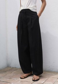 Černé kalhoty s širokými nohavicemi a záhyby, vyrobené z hladké látky. Mají boční kapsy a nosí se s plochými sandály. Lehký a casual design.