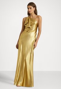 Auksinė satino maxidress su viena peties dizainu ir dideliu kaspinu ties iškirpte. Audinys blizga ir yra švelnios tekstūros.