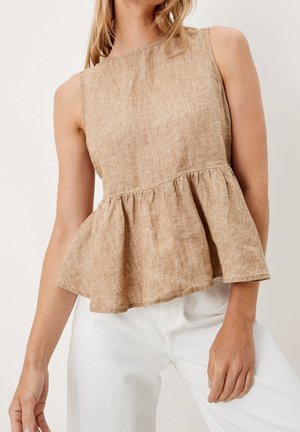 Ærmeløs beige hør top med en opsamlet peplum talje båret med hvide bukser på en person mod en ensfarvet baggrund.