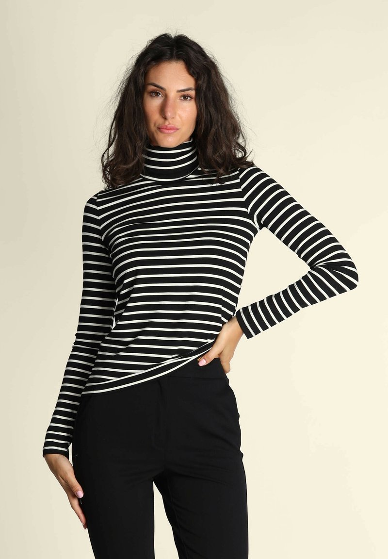 Maglione a collo alto a righe bianche e nere con maniche lunghe; texture morbida e design aderente abbinato a pantaloni neri.