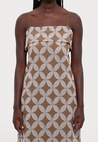 Brown sleeveless dress with white circular pattern, featuring thin straps and a relaxed fit. Material appears smooth with slight texture.