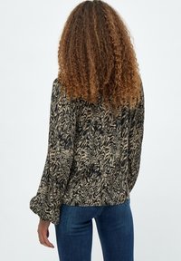Blusa a maniche lunghe con un motivo vorticoso in nero e beige, caratterizzata da una vestibilità comoda e maniche svasate, indossata con jeans blu.