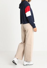 Marinhårig kort hoodie med röda och vita accenter, i kombination med högmidjade beigefärgade vida byxor och vita sneakers. Slät textur.