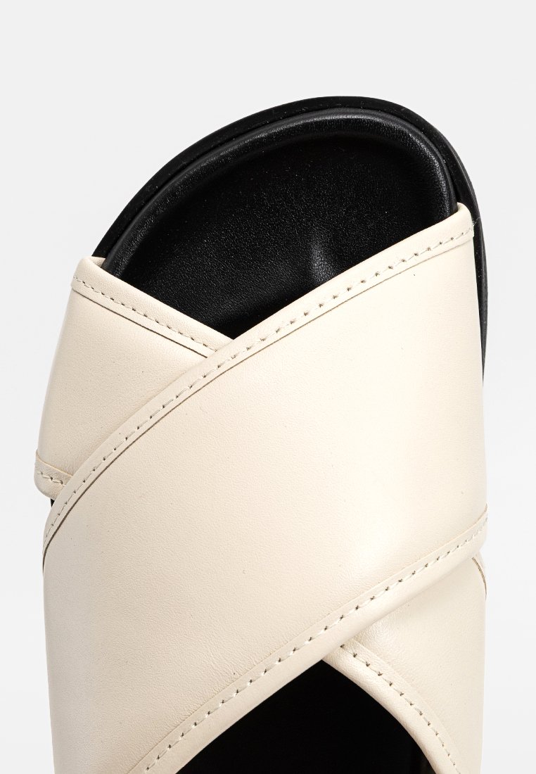 Sandale en cuir beige à glissière avec des brides croisées, empeigne texturée et semelle noire rembourrée. Présente des détails de couture visibles.