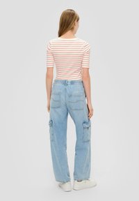 Gestreepte shirt in crèmekleur en koraal, gecombineerd met lichtblauwe cargo jeans met wijde pijpen en flapzakken in een ontspannen pasvorm. Witte sneakers.