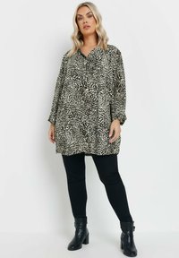 Blusa oversize con stampa leopardata, maniche lunghe, frontale con bottoni e vestibilità comoda, abbinata a leggings neri e stivali alla caviglia.