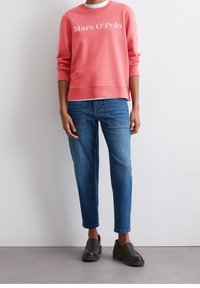 Koraliowy sweatshirt z białym logo "Marc O'Polo", w połączeniu z jasnoniebieskimi prostymi dżinsami i czarnymi butami wsuwanymi, o minimalistycznym designie.