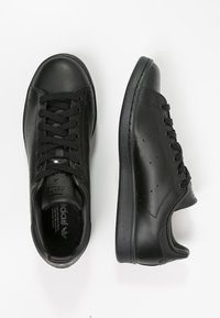 Svarta lädersneakers med en slät yta, utrustade med gummisulor, snörningsdesign, små perforeringar och diskret varumärkning på tungan.