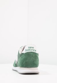 Gröna mocka- och lädersneakers med en vit mellansula och "new balance"-logotyp på hälen i grönt. Klassisk löparsko-design.