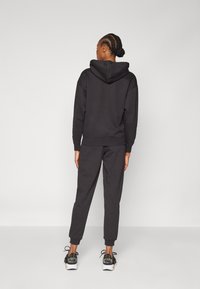 Black hooded sweatshirt and pants set, relaxed fit, made of soft fabric. Features ribbed cuffs and a drawstring hood. Black sneakers with accents.