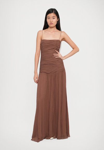 Brown, floor-length dress with ruched texture, spaghetti straps, and flowing skirt. Soft fabric creates a light, draped appearance.