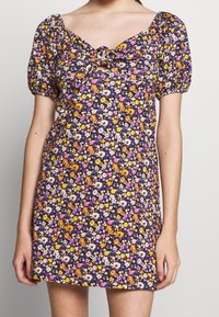 Kwiatowa mini sukienka na ciemnogranatowym tle, z fioletowymi, żółtymi i pomarańczowymi kwiatami. Krótkie, bufiaste rękawy oraz wiązany detal z przodu.