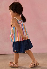 Multicolored striped tank top with embroidered accents, paired with denim shorts featuring orange fruit design, and light pink strappy sandals.