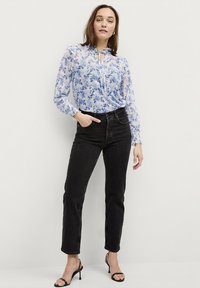 Himmelbluse mit floralen Mustern, Rüschendetails an den Ärmeln und einem Schlüsselloch-Ausschnitt, kombiniert mit hochtaillierten schwarzen Denim-Jeans und schwarzen Riemchen-Heels.