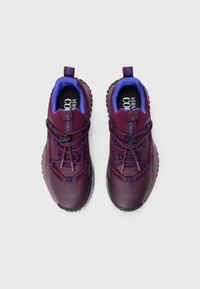 Pair of maroon athletic shoes with blue lining and black cleated soles, featuring toggle-secured laces and brand text on tongue.