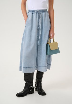 Light blue denim maxi skirt with elastic waistband, side pockets, and a straight cut; paired with black knee-high boots and a small handbag.
