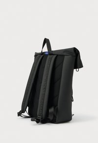 Μαύρο σακίδιο πλάτης με ρολό κλεισίματος, επενδεδυμένη πλάτη, ρυθμιζόμενους ιμάντες ώμου και επάνω χερούλι, εμφανιζόμενο σε απλό φωτεινό φόντο.