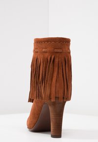 Czekoladowe zamszowe botki za kostkę z frędzlami, falbaniastym brzegiem i smukłą, wysoką szpilką. Gładka faktura i zamknięty tył.