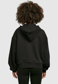 Svart oversized hoodie med en lös passform, utrustad med en dragsko för huvan och ribbade ärmslut. Tyget verkar mjukt med en texturerad yta.