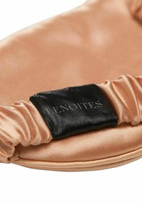 Saténový vlasový doplněk v broskvové barvě se skládacími okraji a černou látkovou visačkou se nápisem "LENOITES." Hladký povrch, jemný a flexibilní design.