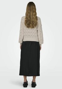 Sweter w kolorze jasnego beżu z teksturowanymi wzorami w kształcie diamentów, w połączeniu z czarną długą spódnicą i masywnymi czarnymi butami, widok z tyłu.