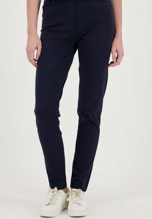Donkerblauwe slim-fit pants van stretchstof, met een platte voorkant, zijzakken en een gladde textuur, gecombineerd met witte sneakers.