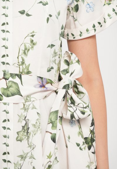 Jurkje van stof met bloemenpatroon, versierd met groene klimop en blauwe bloemen. Het heeft een strikceintuur en korte, opgerolde mouwen. Licht en soepel van textuur.