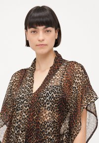 Prozračna bluzica kimono stila s uzorkom leopard printa u smešnim, crnim i bež tonovima, s V izrezom i širokim rukavima.
