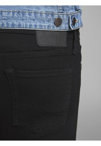 Jeans de mezclilla negros con un diseño de bolsillo trasero curvado y un parche de cuero sobre la cintura. Incluye una chaqueta de mezclilla azul claro.