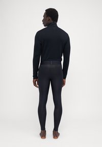 Schwarzes Sportoberteil und figurbetonte Leggings aus glattem Material, mit hohem Kragen und minimalistischem Design, von hinten gesehen.