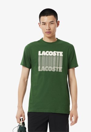 Groene katoenen t-shirt met een witte verticale gestreepte "LACOSTE" logo op de voorkant. Korte mouwen en een ronde hals ontwerp.