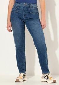 Tmavě modré džíny z denimu se střihovým designem rovného nohu, obsahující přední kapsy, prošívané detaily a opotřebovaný vzhled. V kombinaci s bílými a oranžovými sneakers.