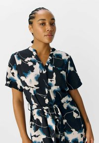 Robe noire avec un motif floral abstrait bleu et blanc, manches courtes, boutonnière à l'avant, col et taille à nouer pour un ajustement réglable.