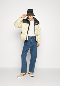 Pufferjack in crème en zwart, met een ritssluiting en zijzakken. Gekozen bij losse blauwe jeans en geruite instappers.