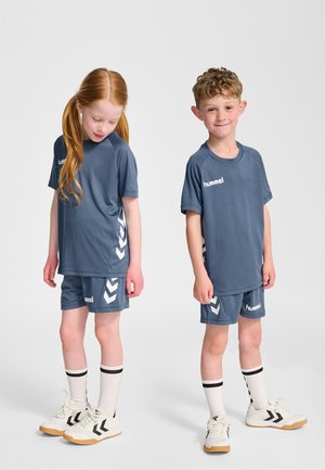 To børn iført matchende blå sportstøj. Overdelen har korte ærmer og mærket "hummel." Shortsene har chevron-accenter.