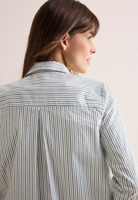 Camicia a maniche lunghe a righe in azzurro chiaro e bianco, con colletto, piega sul retro e tessuto di cotone morbido, in vista laterale.