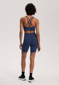 Tengeréskék sportmelltartó, keresztbe álló pántokkal és passzoló, magas derekú rövidnadrággal, amely sima, rugalmas anyagból készült, finom logó részlettel.