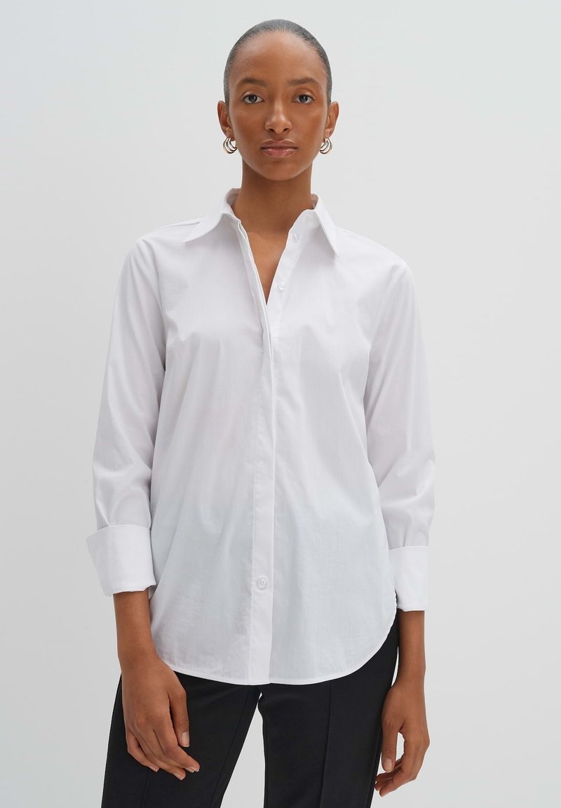 Camicia bianca, colletto button-down, maniche lunghe con polsini arrotolati, texture in cotone liscio, orlo curvo, design minimale, stile classico.