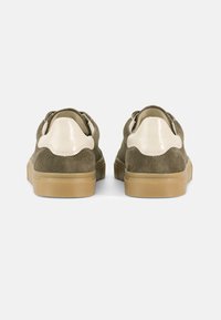 Πράσινα σουέντ αθλητικά παπούτσια με ανοιχτόχρωμες δερμάτινες λεπτομέρειες, στρογγυλεμένη μύτη και υφασμένη ταμπά λαστιχένια σόλα. Η πίσω όψη δείχνει σκαλοπατιαστές λεπτομέρειες.