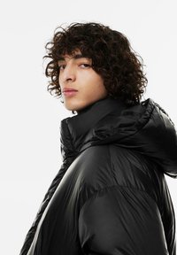 Czarna kurtka puchowa z wysokim kołnierzem i kapturem, charakteryzująca się błyszczącą, gładką teksturą oraz dopasowanym krojem.