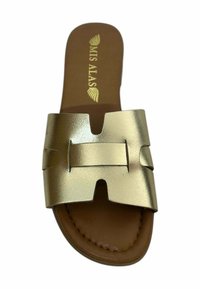 Sandalia plana metálica dorada con una correa ancha que presenta un diseño con recortes. Plantilla marrón con la marca "MIS ALAS". Suela plana. Textura suave.