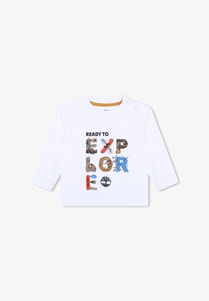Camisa blanca de manga larga con un gráfico multicolor "LISTO PARA EXPLORAR", que incorpora diversas texturas y objetos ilustrados.
