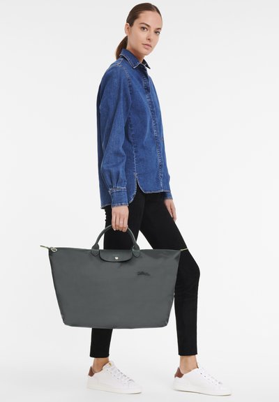 Large gray tote bag with dual handles, featuring a smooth texture and a small logo. Styled with a green zipper accent at the top.