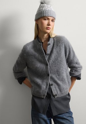 Gray wool cardigan with a soft texture, button closure, and rolled sleeves, layered over a dark shirt. The model wears a matching gray knitted hat.