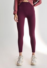 Bordeauxrote, gerippte Leggings mit hohem Bund, kombiniert mit hellen Sneakern. Der Stoff hat eine strukturierte Oberfläche und sitzt eng an.