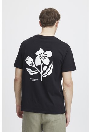 Black cotton t-shirt featuring a large white floral design on the back, with text below the graphic. Short sleeves and crew neckline.