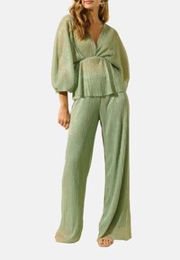 Ensemble bi-matière plissé vert clair comprenant un blouse à col en V profond avec des manches oversized et un pantalon ample. Texture douce et scintillante.